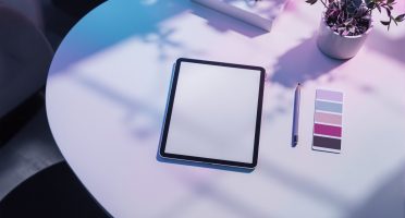 Minimalist workspace with a digital tablet, color swatches, and pencil under soft gradient lighting, representing book cover design and illustration services.